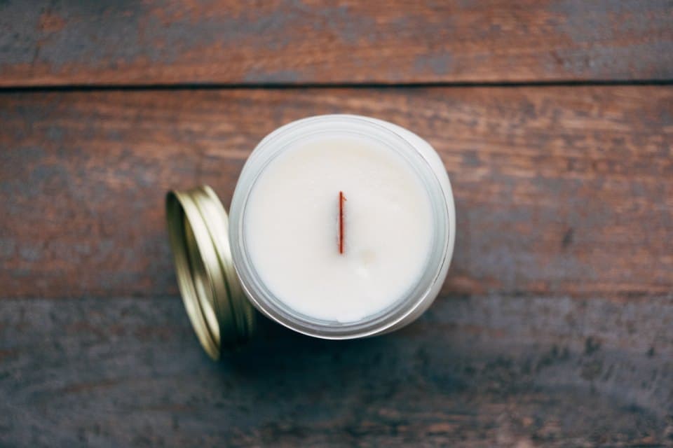 White beeswax candle in a mason jar with a wooden wick and a gold lid beside it
