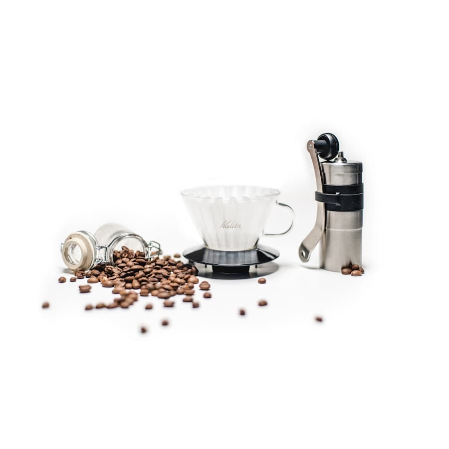Stainless manual coffee grinder beside a glass pour-over dripper and coffee beans