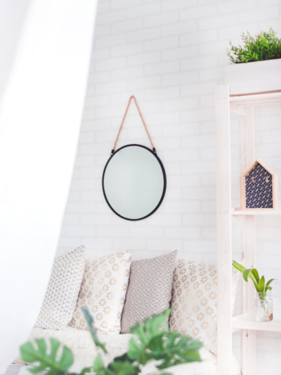 Round wall mirror with a thin black frame hanging from a leather strap