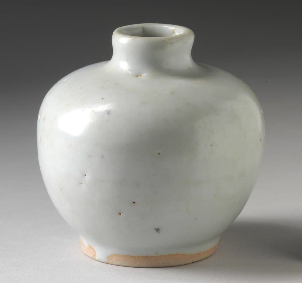 Small round celadon ceramic jar with a pale glaze and unglazed foot