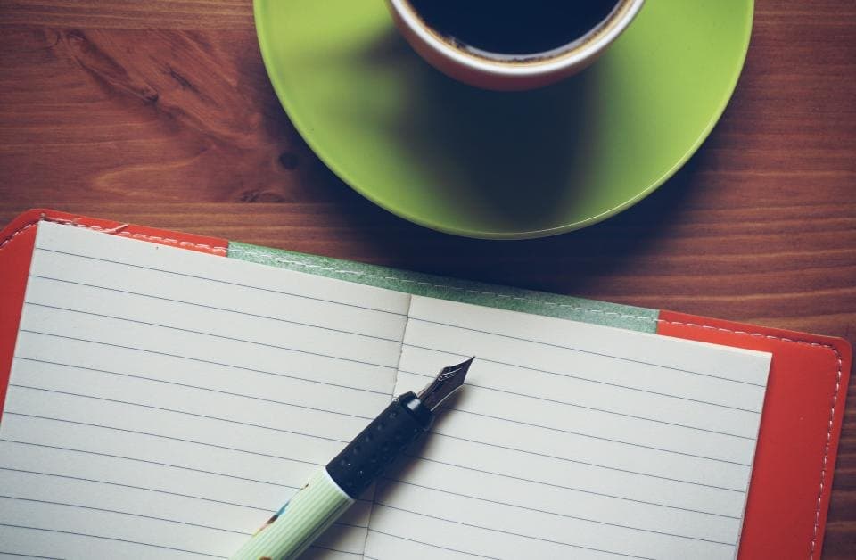Open lined journal with a fountain pen beside a cup of coffee