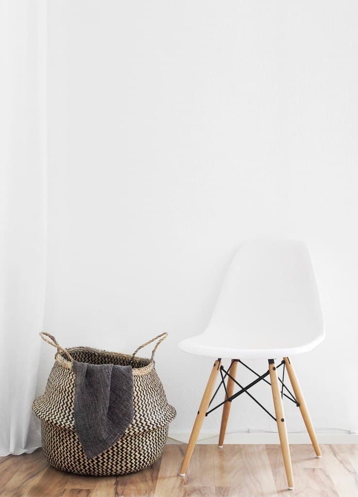Tall seagrass belly basket with handles beside a white chair, holding a folded throw