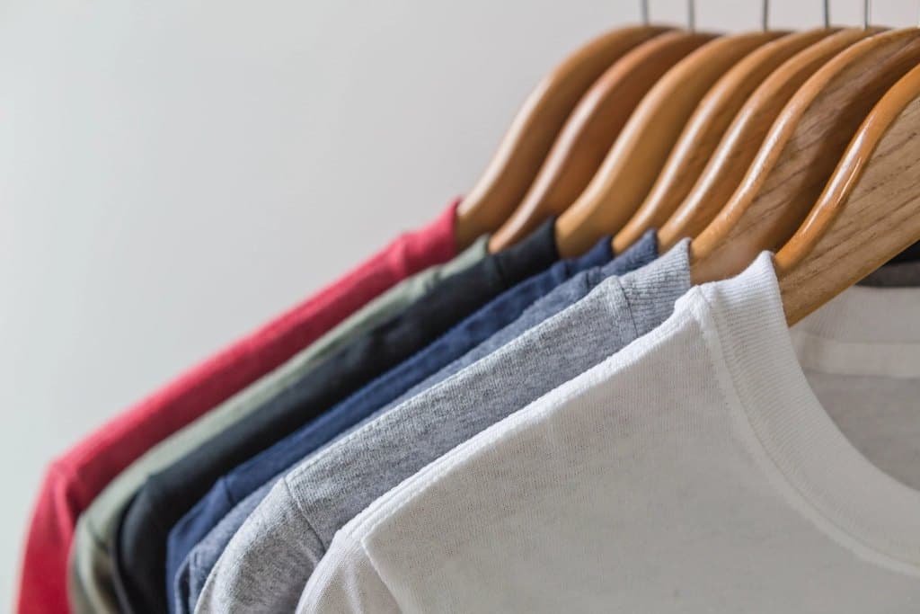 Row of organic cotton crewneck tees hanging on wooden hangers in mixed colors