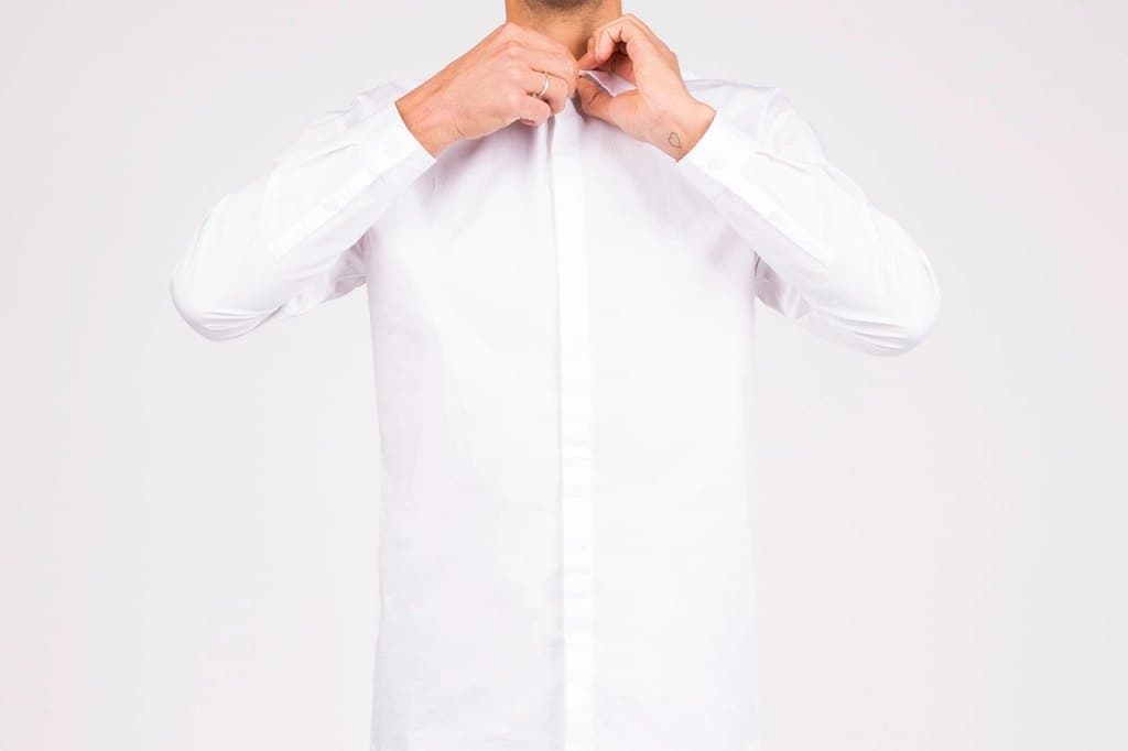 Person fastening the collar of a white cotton poplin day shirt