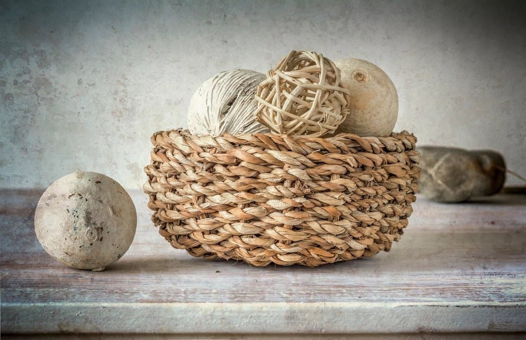 Small braided seagrass catchall basket holding yarn balls on a painted wood surface