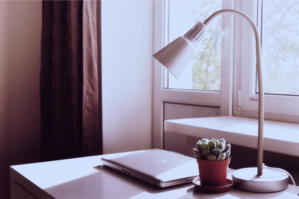 White gooseneck desk lamp beside a laptop on a sunlit desk